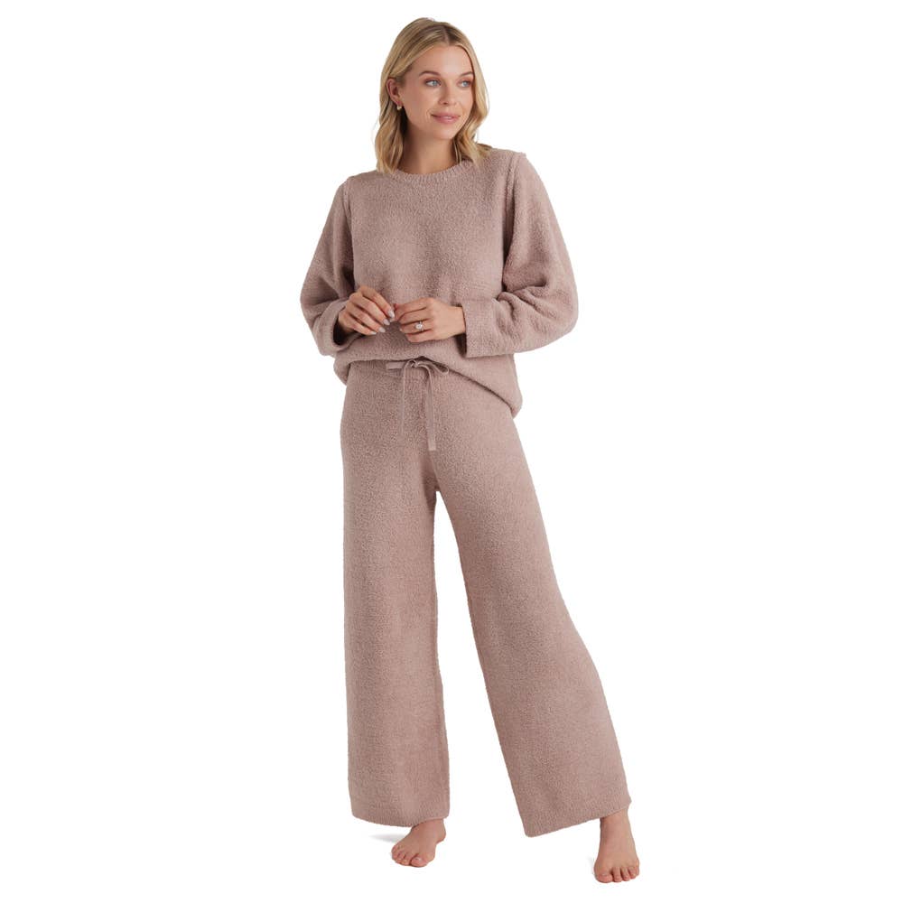 A person is standing barefoot in the Marshmallow Lounge Set, a cozy light brown women’s set known for its unmatched softness. It features a knit sweater and matching wide-leg pants. Their hands are relaxed by their sides, and the outfit appears perfect for lounging, exuding comfort against the plain white background.