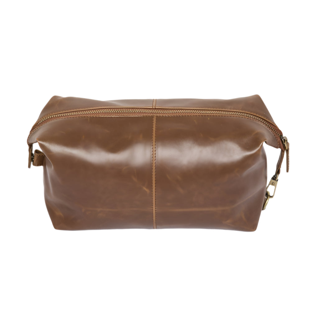 The Journeyman Dopp Kit, crafted from brown vegan leather, showcases a classic design with a visible top zipper. Its central seam and subtly worn texture give it a vintage charm, while metal zipper pulls enhance its appeal. Ideal for holding grooming essentials, it sits elegantly on a plain white surface.
