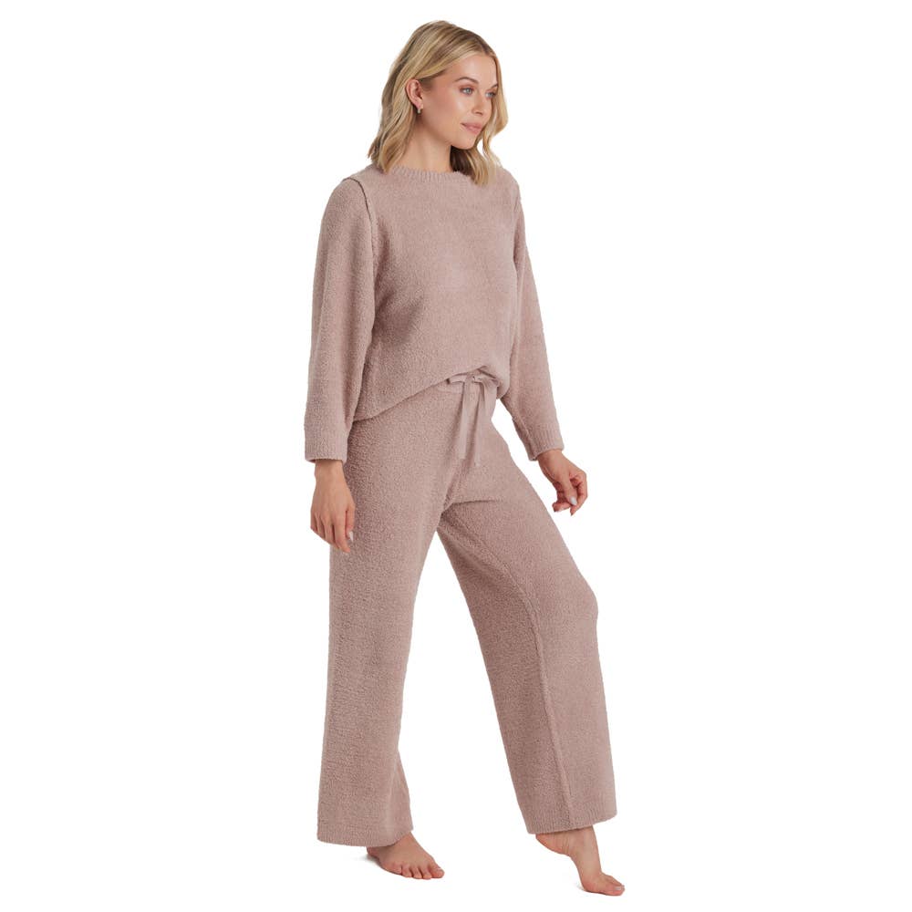 A woman with shoulder-length blonde hair is wearing the Marshmallow Lounge Set, a taupe ensemble celebrated for its unmatched softness and endorsed by Oprah. The cozy matching outfit includes a long-sleeve sweater and wide-leg pants with a drawstring waist. She stands barefoot on a white background, gazing to the side.