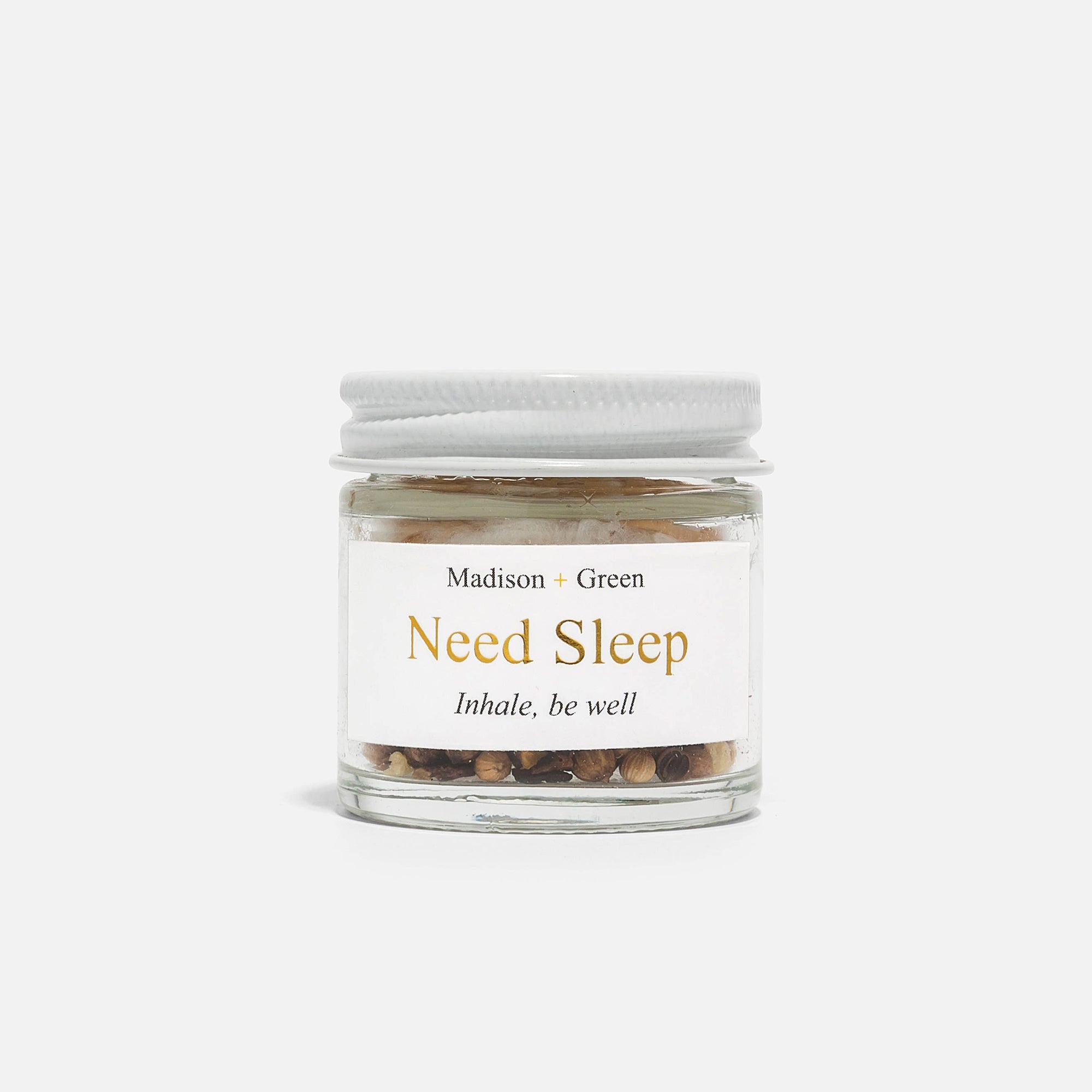 A small glass jar labeled "The Essentials" from Madison + Green, featuring stress-relieving scents and a blend of dried herbs, with a white screw-on lid. The tagline "Inhale, be well" graces the simple white background, inviting you to explore soothing aromatherapy inhalers.