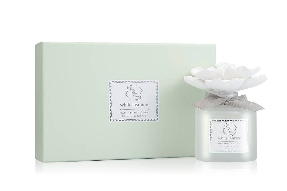 The Marigold Ceramic Flower Diffuser Gift Set - White Jasmine makes an ideal gift. The sophisticated packaging, in a soft light green, displays a label, and the frosted glass diffuser bottle features a white ceramic flower top and a gray ribbon. Both are adorned with "white jasmine" labels framed by decorative borders.