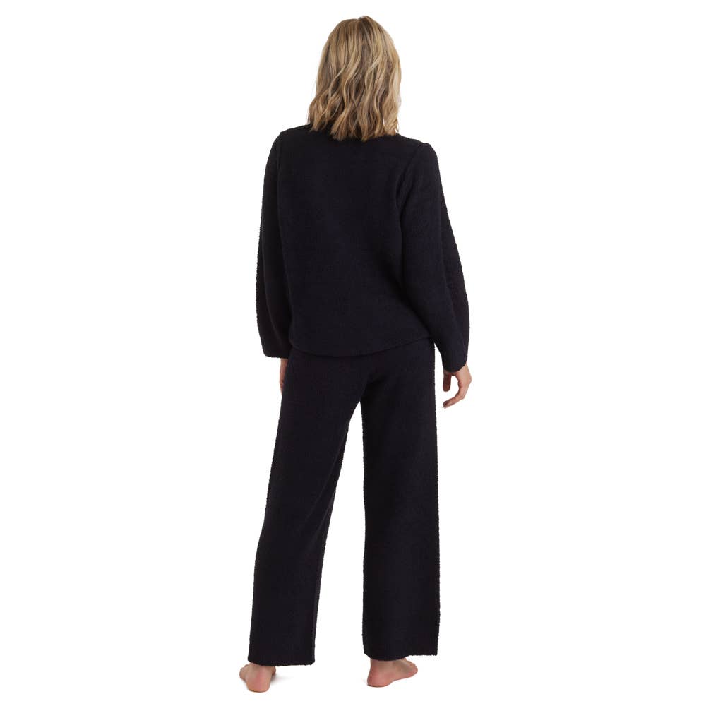 A person with wavy blonde hair stands barefoot, highlighting Oprah's favorite—the Marshmallow Lounge Set, celebrated for its unmatched softness. The coordinating black textured sweater and wide-leg pants embody cozy elegance against a plain white backdrop.