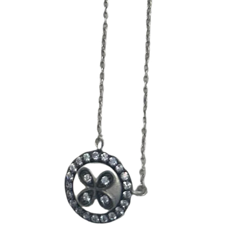 The Clover Necklace, a sterling silver piece, features a clover design at its center surrounded by cubic zirconia for added sparkle. It's displayed against a light gray background, enhancing its elegance.