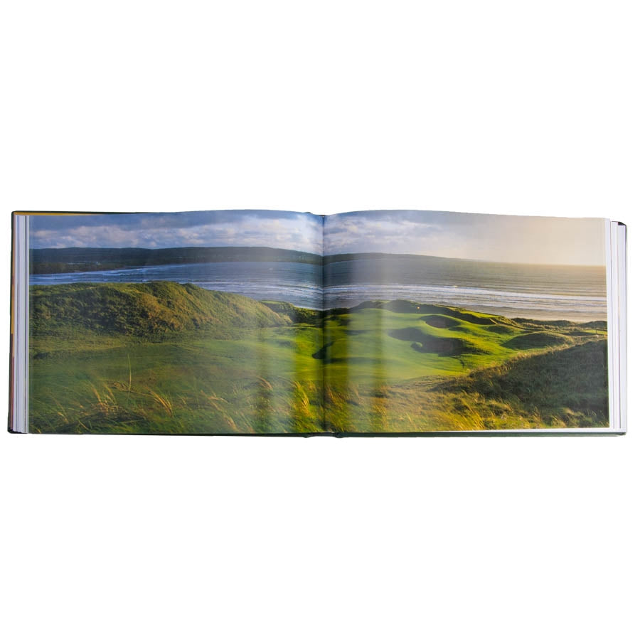 A leather-bound edition of "Golf Courses - Fairways of the World" showcases an expansive photograph by David Cannon, depicting a renowned coastal golf course. The vibrant scenery includes multiple bunkers and a fairway with an ocean view. The horizon is marked by a clear sky dotted with clouds, creating a serene and picturesque atmosphere.