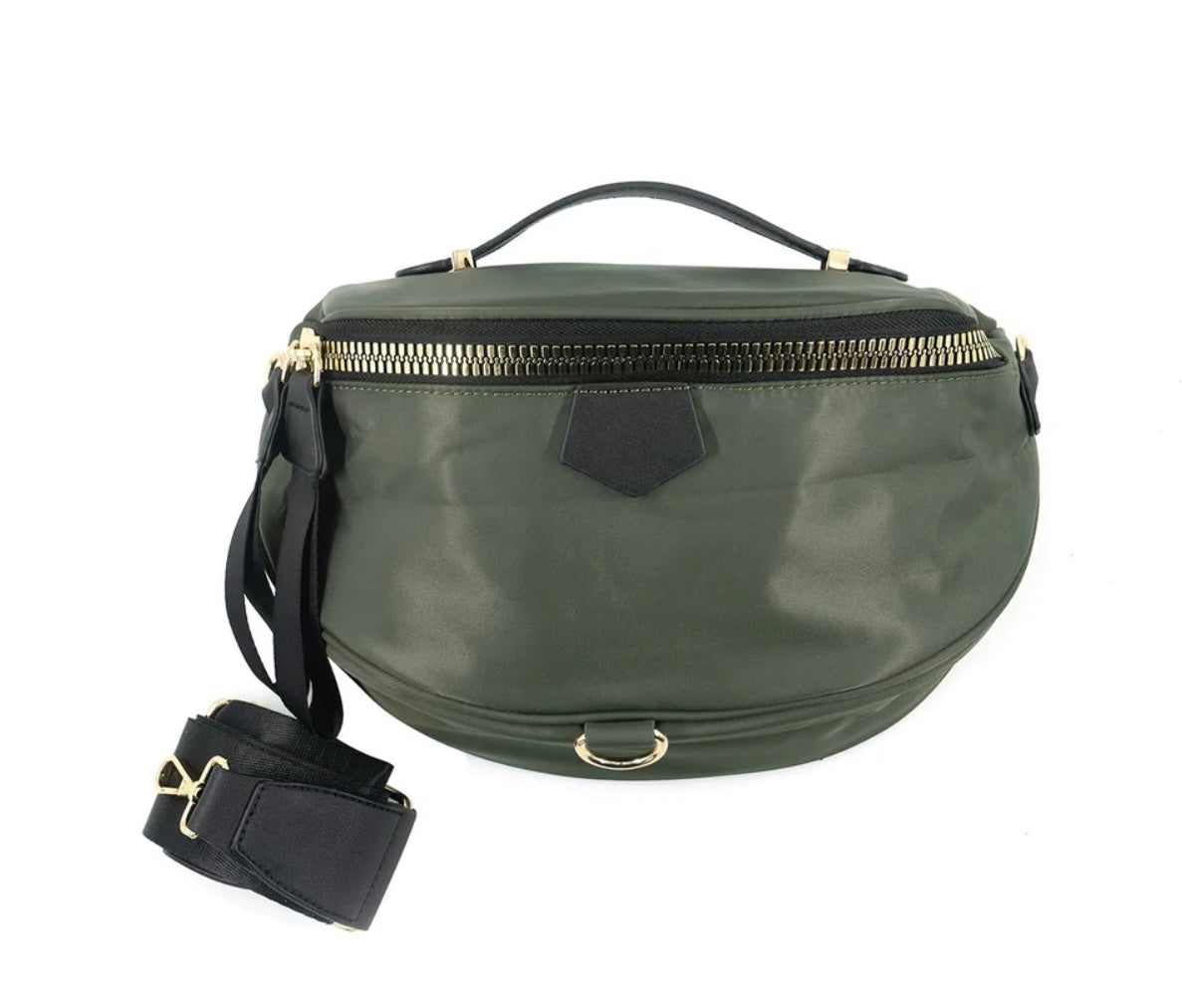 Introducing the Nylon Bum Bag/Fanny Pack: a chic, medium-sized olive green bag crafted from durable nylon. Designed in a trendy crescent shape, it features a gold zipper and is adorned with a black leather handle on top. The detachable black strap and metallic ring detailing at the bottom enhance its modern, versatile appeal.