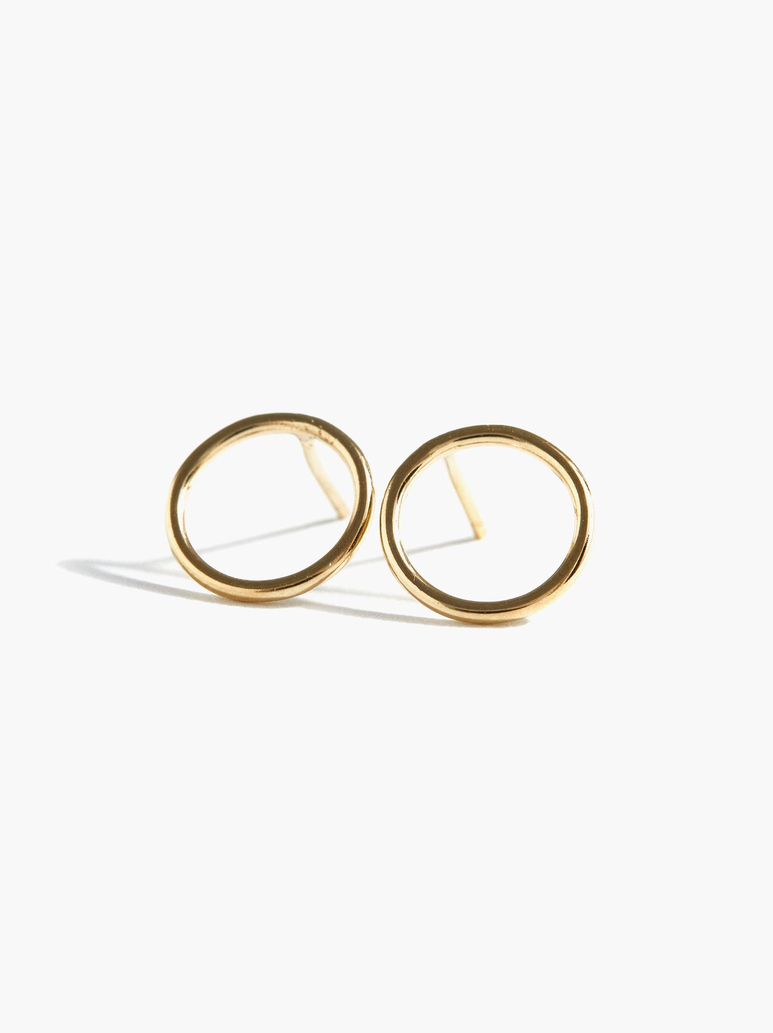 Celine Stud Earrings, featuring a minimalist design with a gold-filled finish, are displayed against a plain white background. These small, circular earrings boast a smooth, polished surface and are ideal as an everyday accessory. They cast soft shadows to the left, enhancing their three-dimensional appearance.