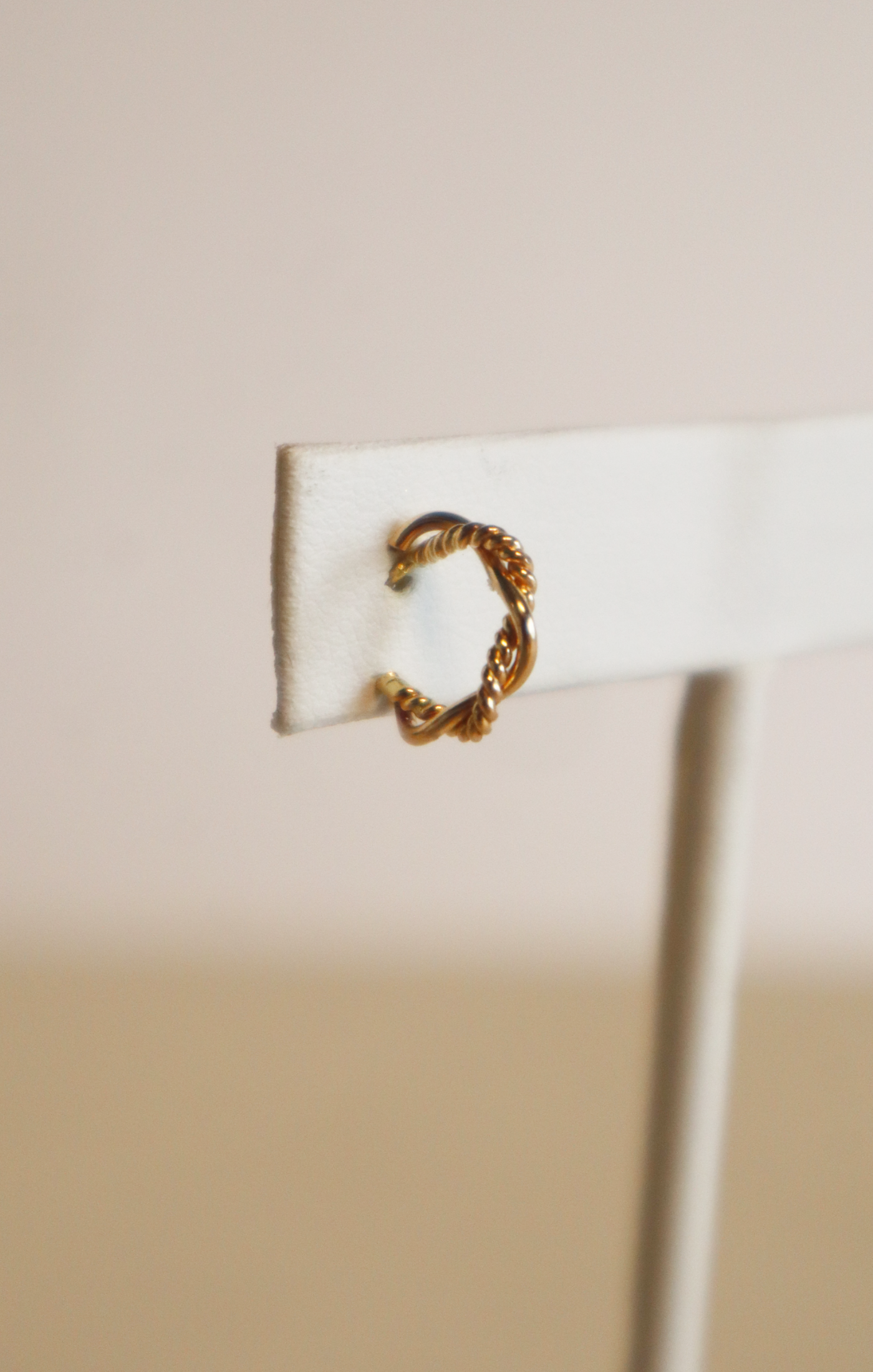 Explore the Braided Mini Hoops, a pair of stunning earrings designed for everyday wear and crafted from 14k gold-filled material. Presented on a white stand with a soft beige background, these hoops feature a rope-like texture and twisted design that offer an intricate yet minimalistic elegance.