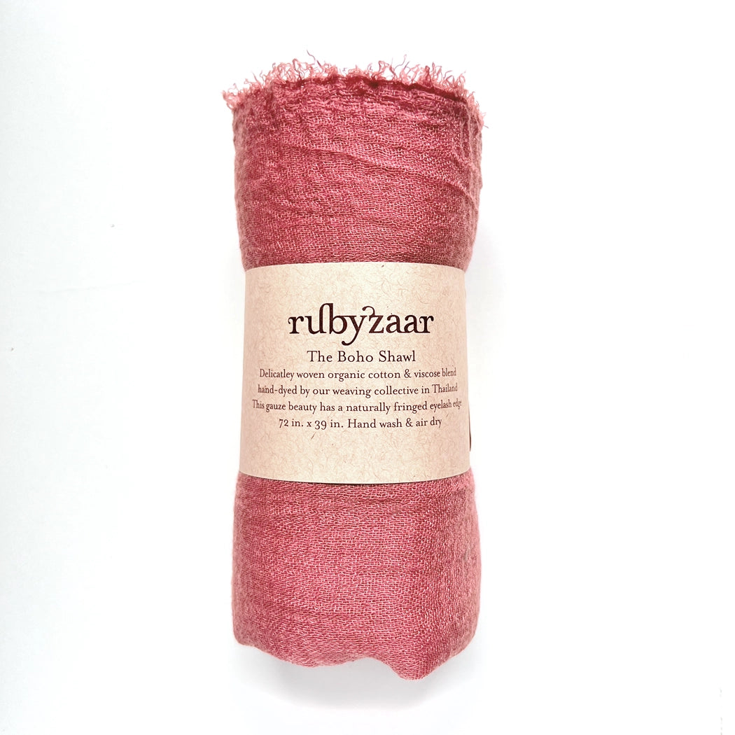 A "Boho Scarf" in a red cotton-viscose blend is rolled and wrapped with a beige paper band labeled "rubyzaar The Boho Shawl." This hand-dyed, bohemian-style accessory was woven in Thailand and features fringed ends. Hand wash and air dry are recommended for care, with dimensions measuring 72 x 39 inches.