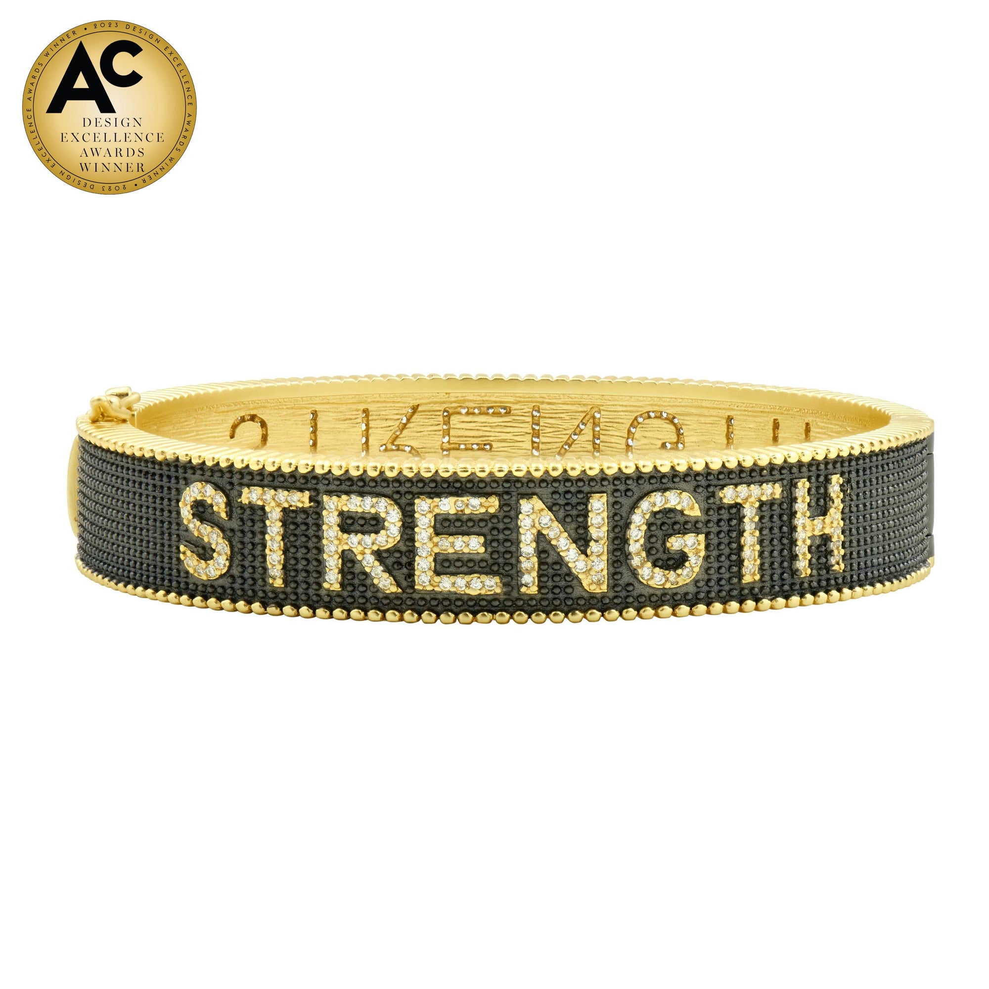 The STRENGTH Bracelet presents a gold design adorned with black beaded detailing and prominently displays "STRENGTH" in bold letters. A gold circular badge situated in the top left corner announces its recognition as an "AC Design Excellence Award Winner." Its intricate and textured pattern exudes premium quality, reminiscent of sterling silver craftsmanship.