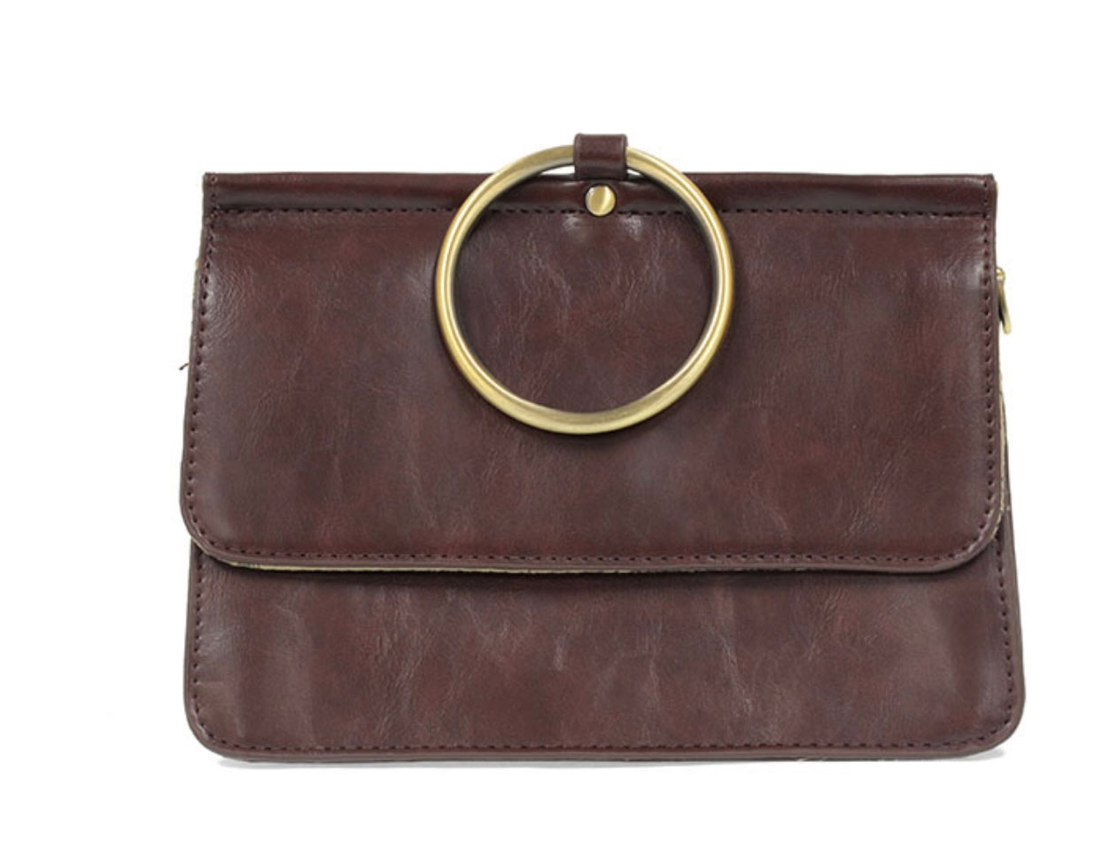 The Aria Ring Bag - Fall/Winter is a brown leather clutch with a large, gold circular handle on the front, reminiscent of a bracelet bag. It features a flap closure and a smooth, polished texture. Its minimalist design is enhanced by the elegant gold ring and includes an optional crossbody strap for added versatility.
