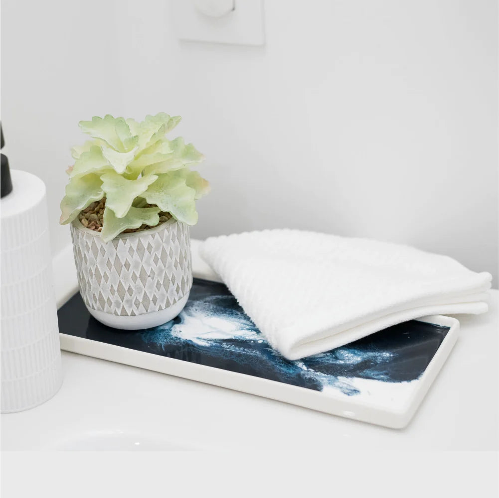 A decorative bathroom setup featuring a small potted succulent with a textured white and grey pot, placed on a Ceramic Resin Tray showcasing a blue and white marbled pattern. Next to the plant are neatly folded white washcloths, creating a clean and minimal aesthetic that elevates your home decor.