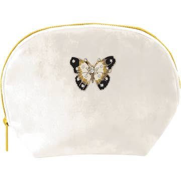 The Clamshell Bag, a small cream velvet pouch with a curved top and yellow zipper, displays an embroidered butterfly in black, gold, and ivory hues accented by rhinestones against a plain white background.