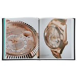 An open copy of *The Book of Rolex* reveals close-up images of a luxury wristwatch, showcasing expert watchmaking craftsmanship. The left page highlights intricate details of the watch face and dial, while the right provides a full view with its metallic strap. The rose gold timepiece appears exquisite against the glossy pages.