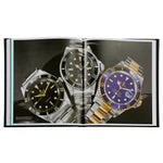 An open volume of "The Book of Rolex" reveals three luxury watches against a dark backdrop. The left and center timepieces, featuring black dials, glisten with silver and gold accents. To the right, a watch with a blue dial dazzles in gold and silver tones. This display is a testament to watchmaking expertise and timeless elegance.