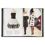 An open copy of the "Little Book of Chanel" reveals stunning style. The left page showcases a timeless black and white strapless dress with a flared skirt, echoing Coco Chanel's iconic elegance. On the right, a runway scene features models flaunting black and white ensembles, including one with chic bow details.