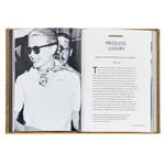 An open copy of "Little Book of Gucci" reveals a black and white photograph of a person wearing sunglasses and a scarf, capturing the timeless essence associated with Gucci. The opposite page presents text under the title "Priceless Luxury," embodying the spirit of Italian fashion. The book is set against a plain white background.
