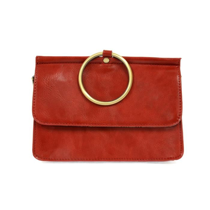 Introducing the Aria Ring Bag - Fall/Winter edition: a chic clutch crafted from smooth red vegan leather. This stylish piece features a striking large gold circular ring on the front flap, enhanced by its minimalist design and visible edge stitching. It also includes an optional crossbody strap for added versatility in its modern appearance.