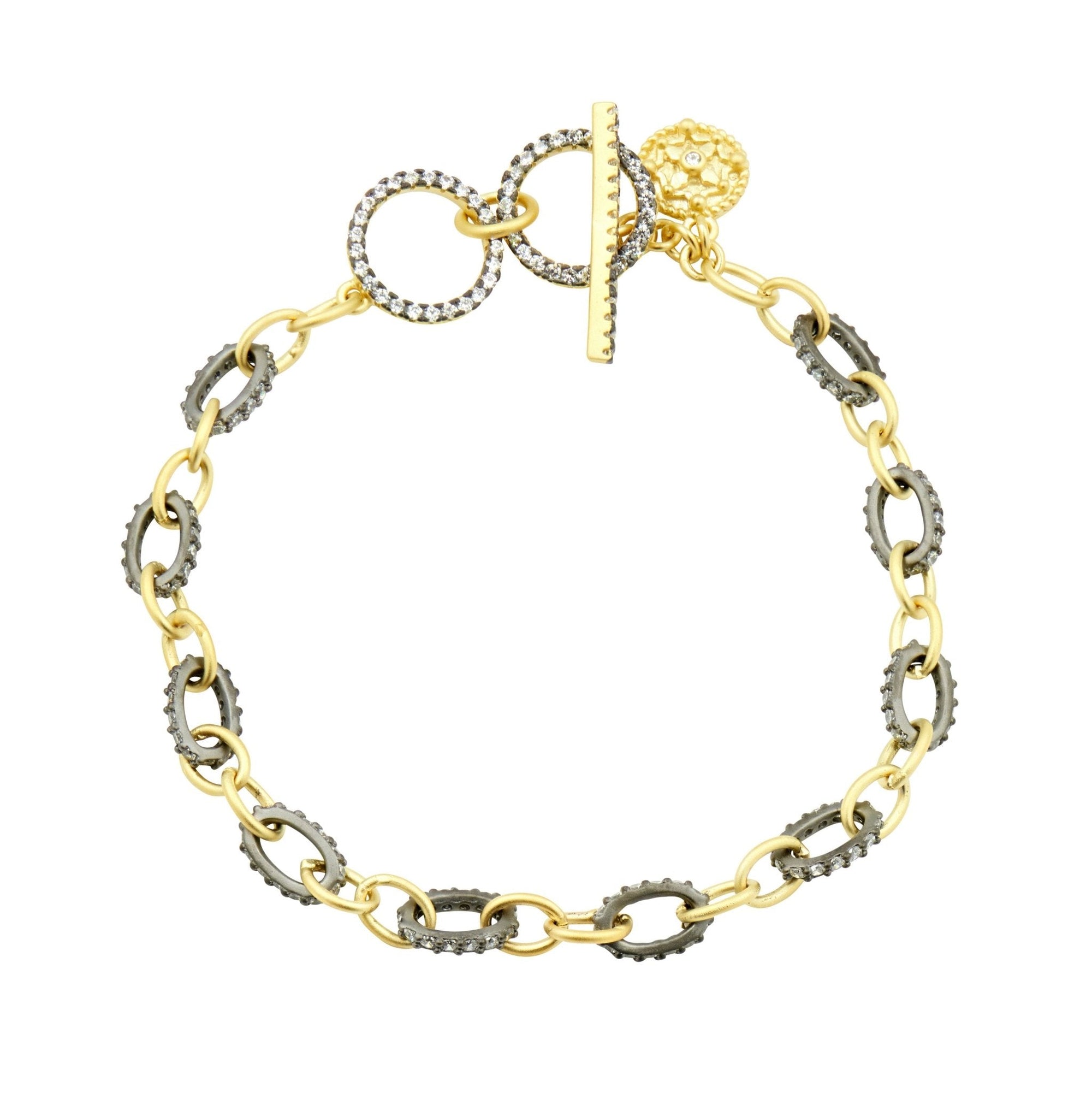 Introducing the Two-Tone Soft Chain Bracelet, a gold and silver piece with alternating circular and oval links. It features a textured toggle clasp, round charm, and ridged links for enhanced sophistication in an elegant 14K gold design that embodies modern style.