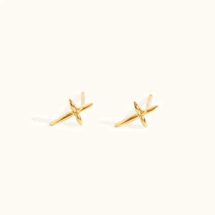 On a light background are two small, gold Droplet Cross Studs, each featuring an elegant polished finish with symmetrical lines creating an "X" shape. Handcrafted in Nashville, these vermeil studs offer a minimalistic design that is ideal for an elegant earring stack suitable for everyday wear.