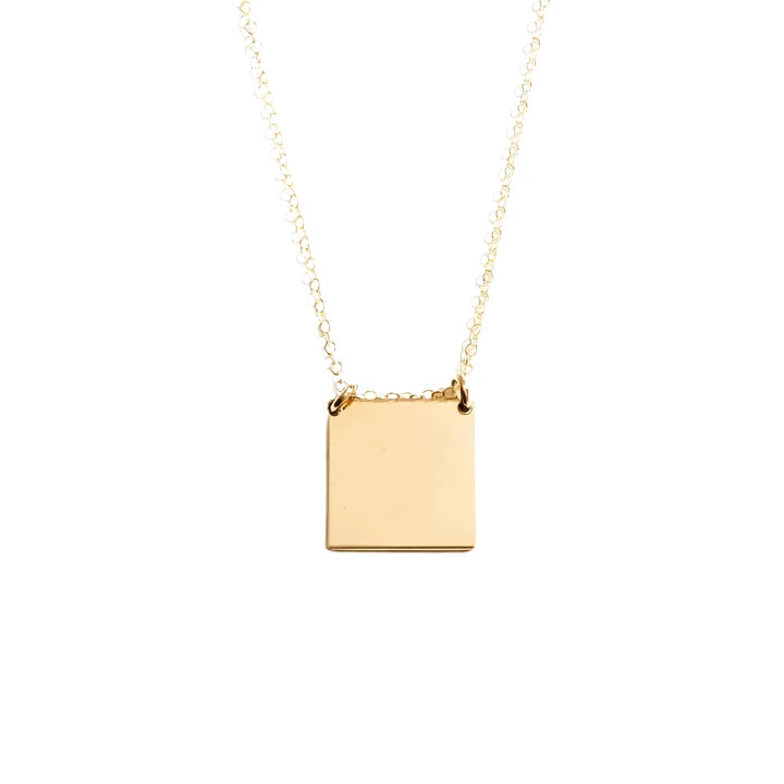 The Phrase Necklace: "you are loved" is a handcrafted jewelry piece featuring a minimalist square pendant on a thin 14k gold-filled chain. It boasts a smooth, matte finish that appears to be made of gold or gold-toned metal. The necklace is elegantly displayed against a plain, light background.