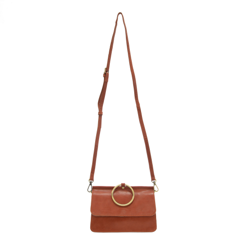 Introducing the Aria Ring Bag - Fall/Winter, a sophisticated brown vegan leather crossbody bag. It features a long adjustable strap secured with gold hardware on each side, complemented by a prominent gold ring on the front flap. Its rectangular silhouette and sleek design exude simplicity and elegance.