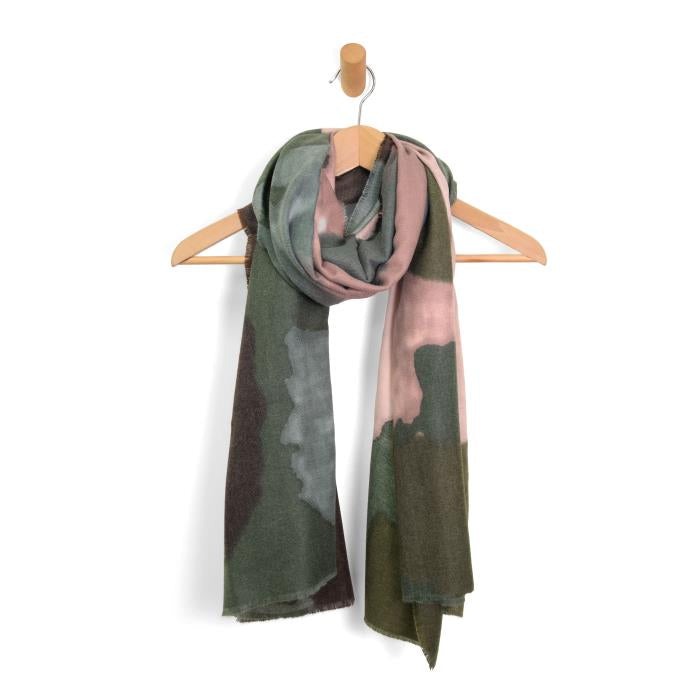A Midweight Patterned Scarf showcasing hues of green, gray, pink, and brown is elegantly draped over a wooden hanger. It features an abstract pattern reminiscent of cheetah spots and sports unfinished edges for a casual touch. The scarf is displayed against a plain white background.