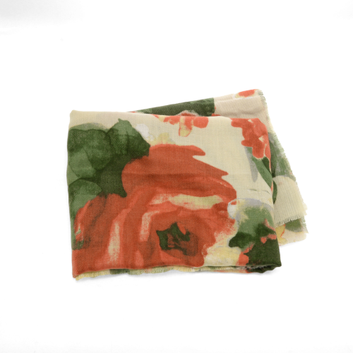 The Midweight Patterned Scarf, featuring oversized red and green floral designs on a cream backdrop, exudes elegance. Its lightweight, slightly sheer fabric drapes beautifully on a plain white surface, highlighting its delicate charm.