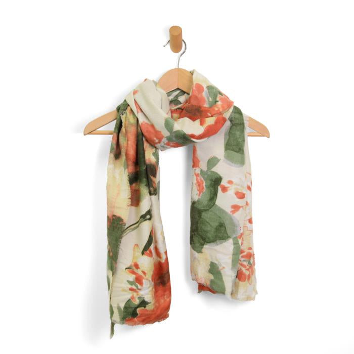 A chic Midweight Patterned Scarf featuring a blend of red, orange, and green hues gracefully hangs on a wooden hanger. The scarf sports an abstract floral design on a cream background, with slightly frayed ends adding a casual touch, elegantly displayed on a simple wall hook.