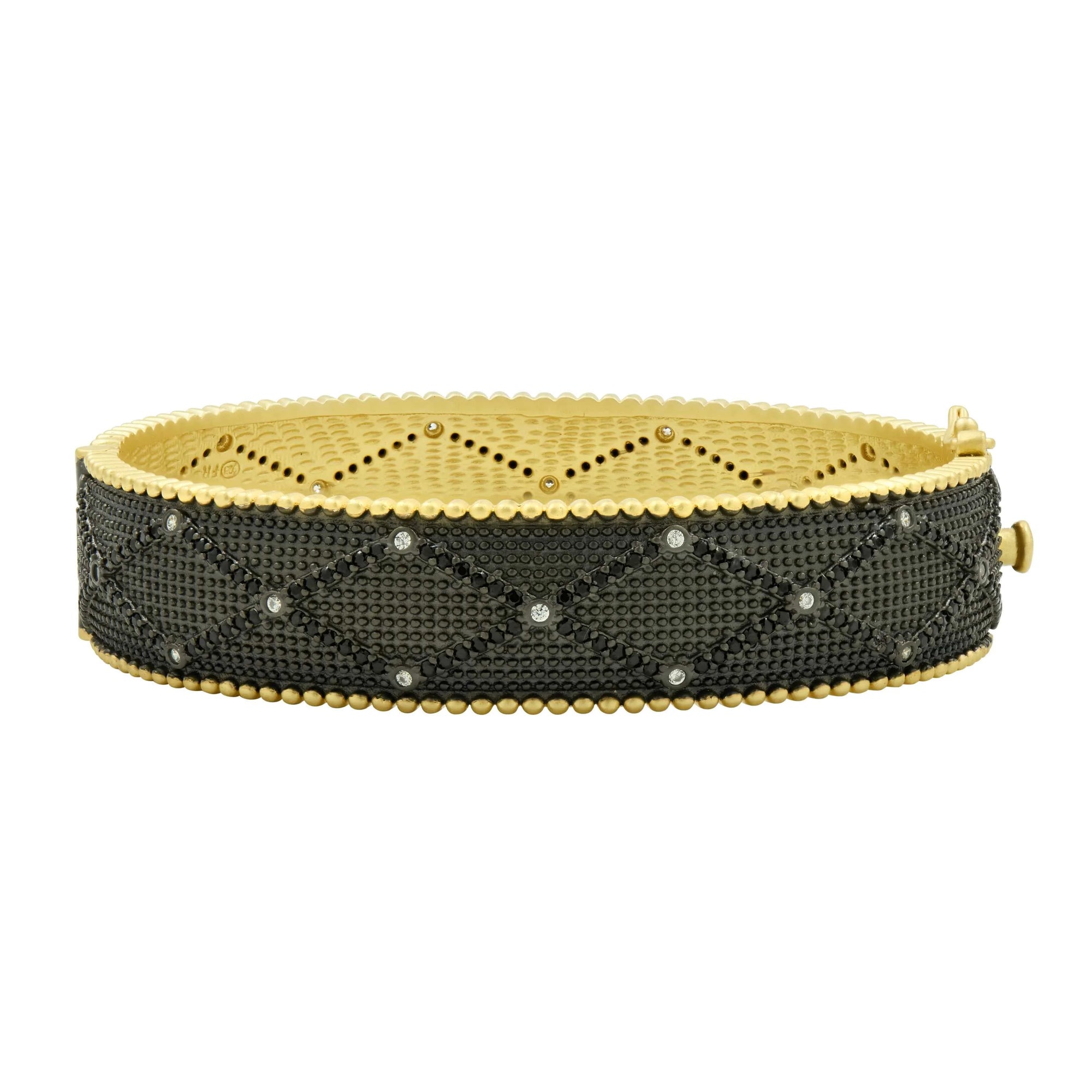 Introducing the Signature Textured Hinged Bangle: a luxurious accessory featuring a 14K gold finish and textured black band. Adorned with Brooklyn Bold crisscross patterns and small silver accents, it boasts an ornate scalloped design along the inner edge. The elegance of black cubic zirconia elevates its allure, while the side-fastened clasp ensures easy wear.