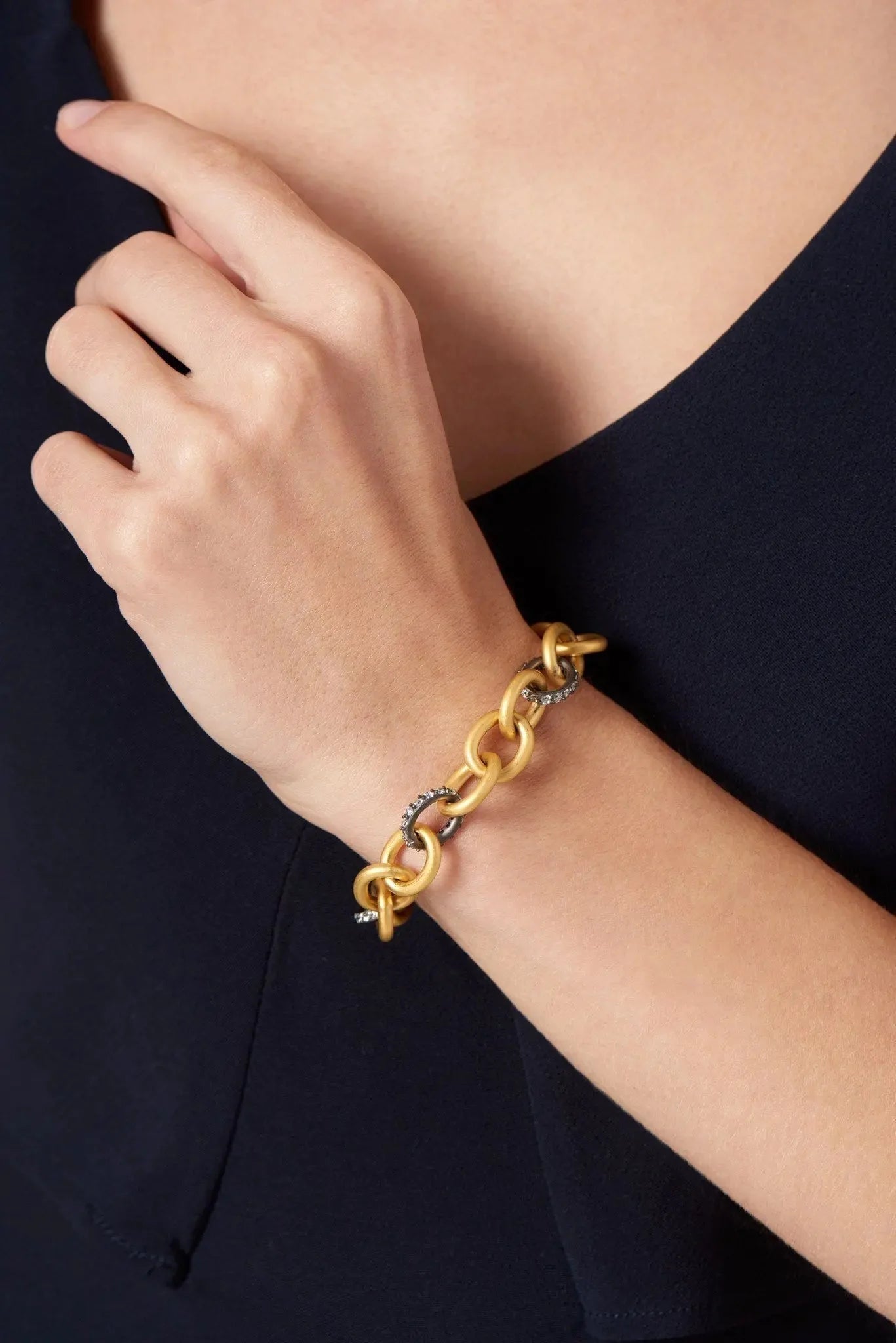 A person with light skin wears the Signature Heavy Link Bracelet, crafted from sterling silver and featuring interlocking links, some embellished with sparkling cubic zirconia. This sophisticated piece rests on their right wrist and softly touches their left shoulder as they wear a dark sleeveless outfit.