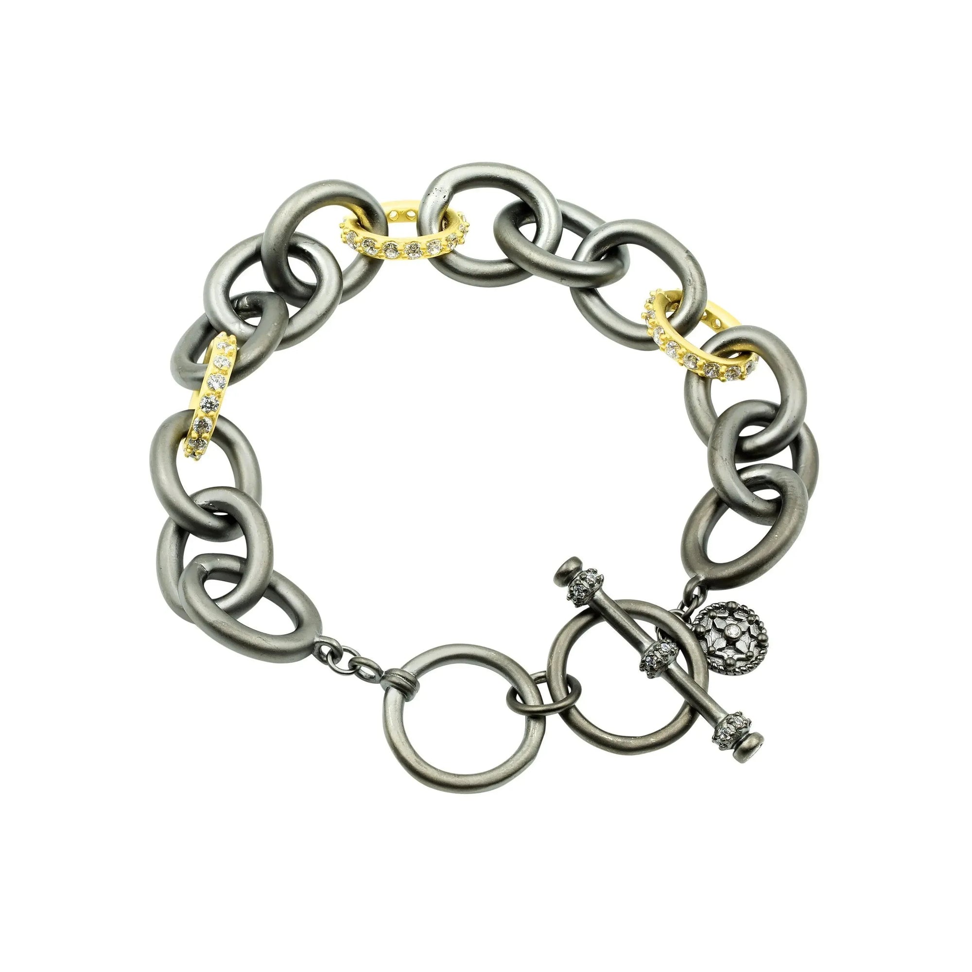 The Signature Heavy Link Bracelet features large, interlocking metal links in alternating dark gray and gold tones. The gold links are adorned with small cubic zirconia gems. It is secured with a round clasp featuring bar and ball details and is complemented by a textured spherical charm.