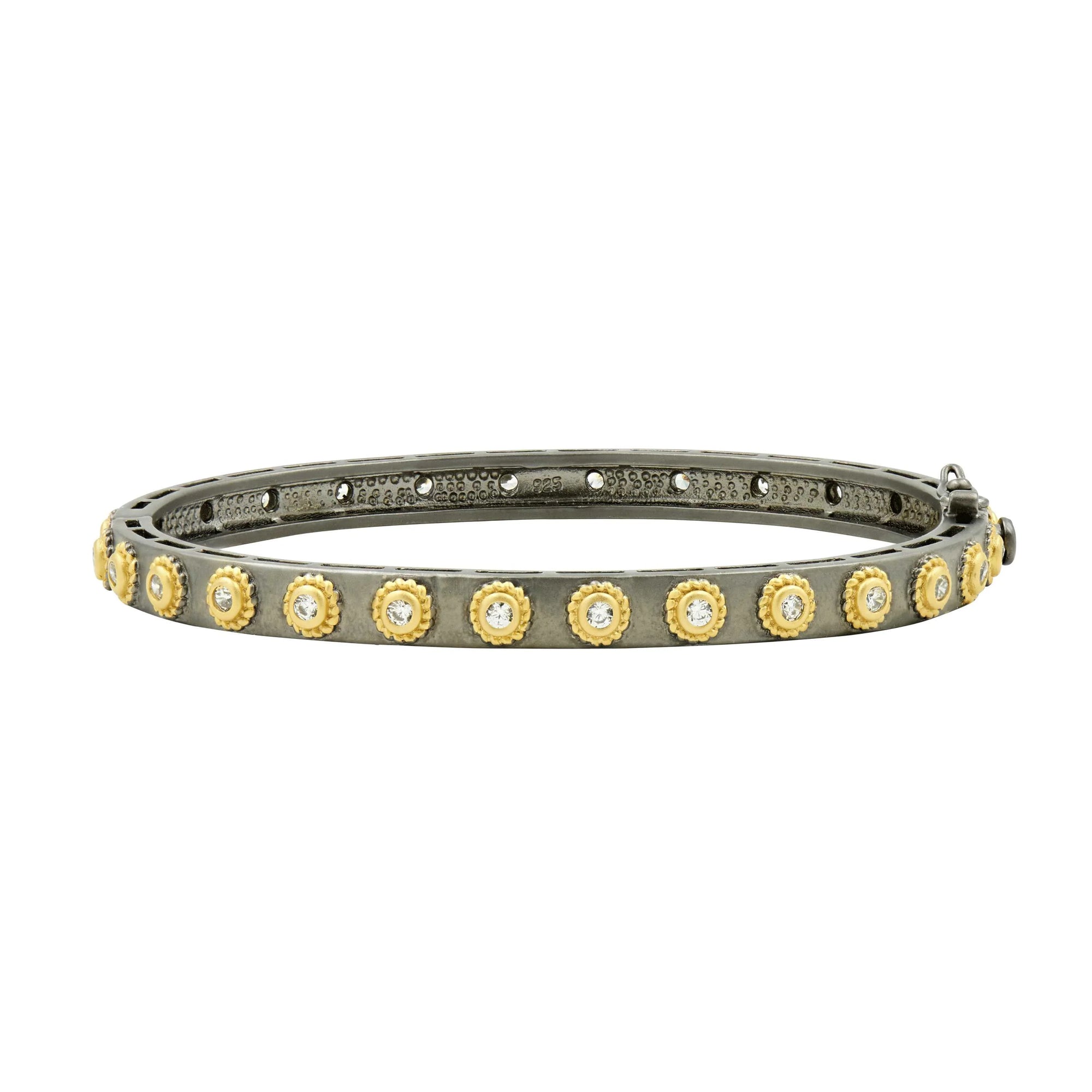The Studded Eternity Hinge Bangle, a slender metal accessory ideal for stacking, showcases a single row of round, yellow gold-toned settings that hold sparkling clear gemstones. It features an antique finish with a subtle, intricate pattern on the inside.