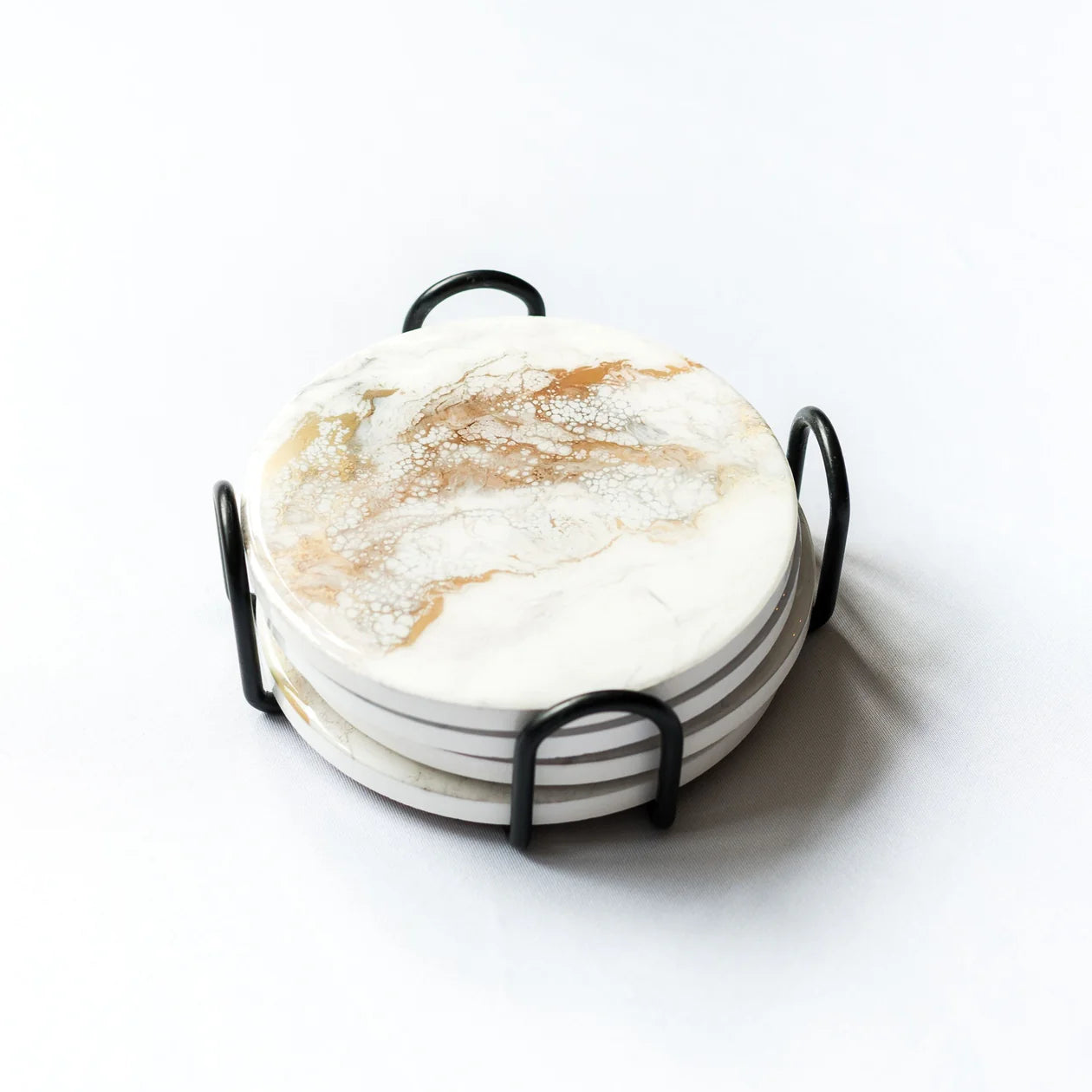 The Ceramic Resin Coaster Set includes four round coasters adorned with gold and white swirling marble-like patterns, neatly stacked in a black metal holder with convenient side handles, set against a simple, light backdrop.