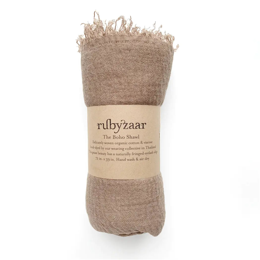 A rolled-up Boho Scarf in a bohemian style, featuring a fringed edge, is wrapped in a label saying "rubyzaar" and "The Boho Shawl." Made from hand-dyed organic cotton viscose and handwoven in Thailand, it includes care instructions to hand wash and air dry.