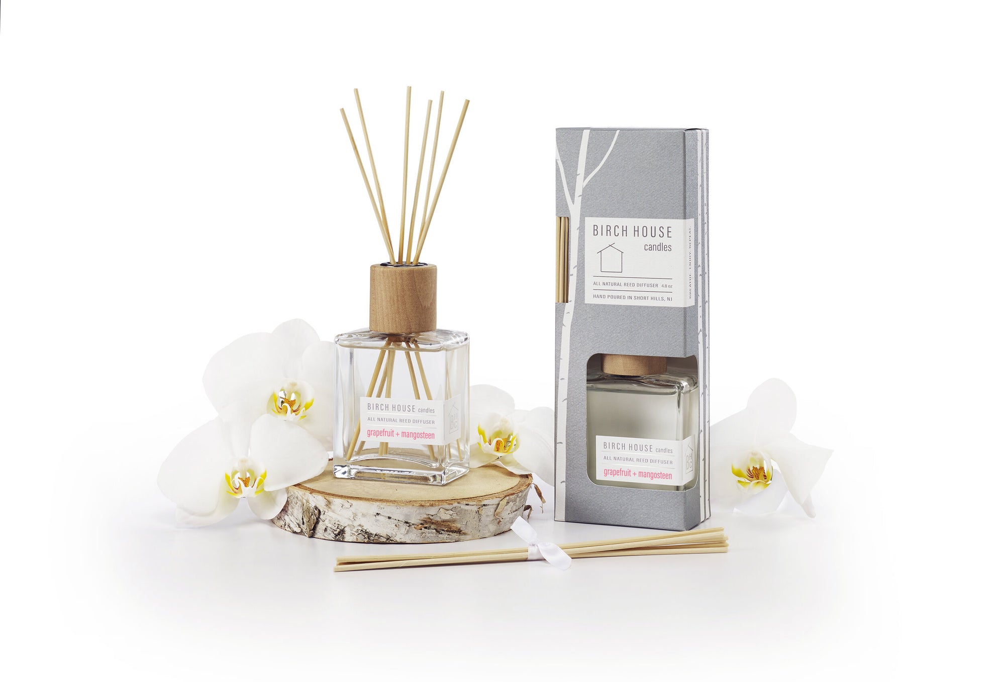 The Sweet Grapefruit Diffuser set includes birchwood reeds in a glass bottle labeled "Birch House Candles," featuring "Patchouli + Lemongrass" essential oils. A matching boxed candle, surrounded by white orchids on a wooden slice, completes the nature-inspired packaging design.