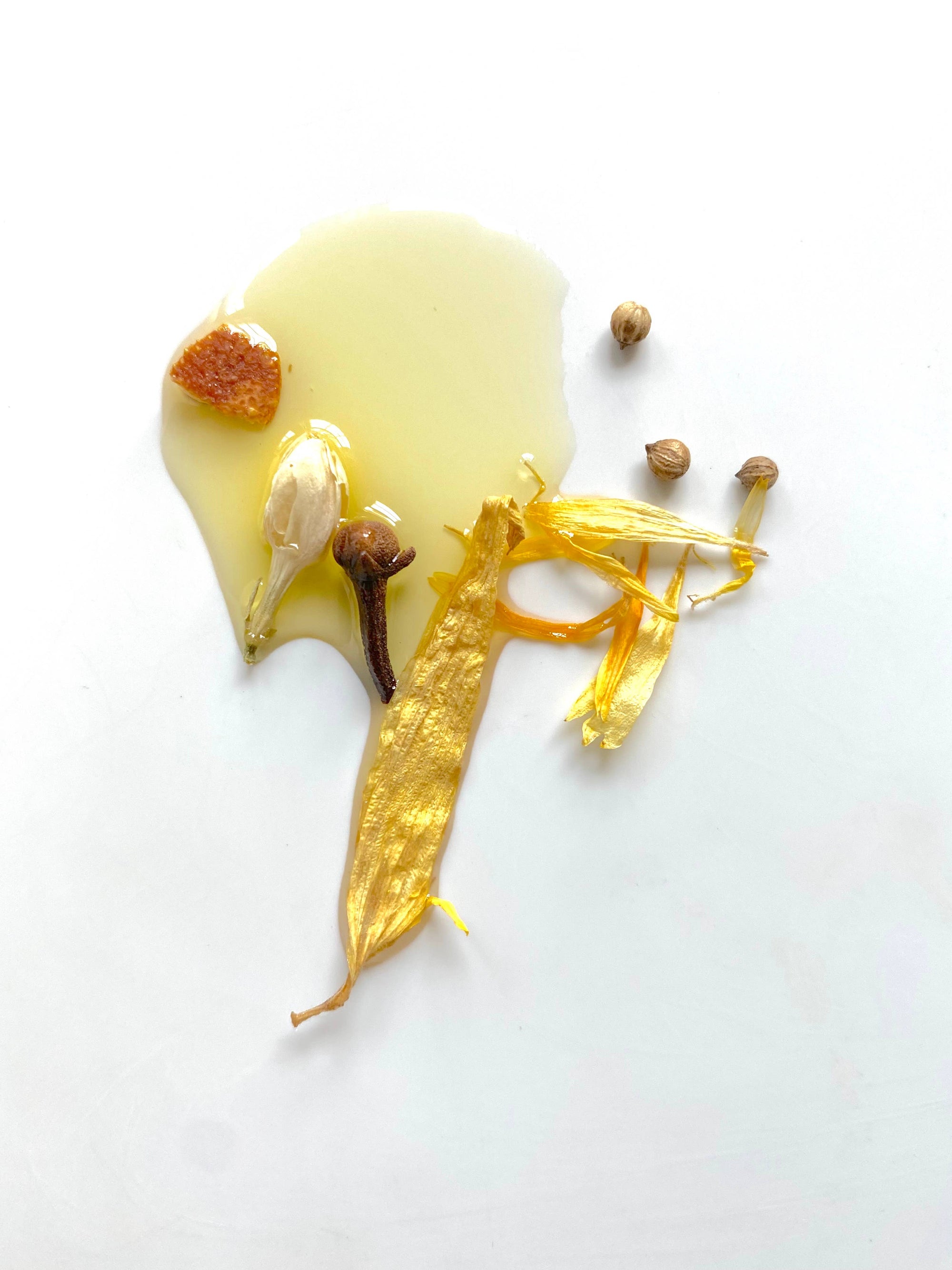 A glossy puddle of honey glistens on a white surface, topped with a garlic clove, a piece of dried orange, a clove, and a golden leaf surrounded by scattered small seeds. This natural arrangement evokes the therapeutic aroma reminiscent of "Need Sleep" - Aromatherapy Body Oil.