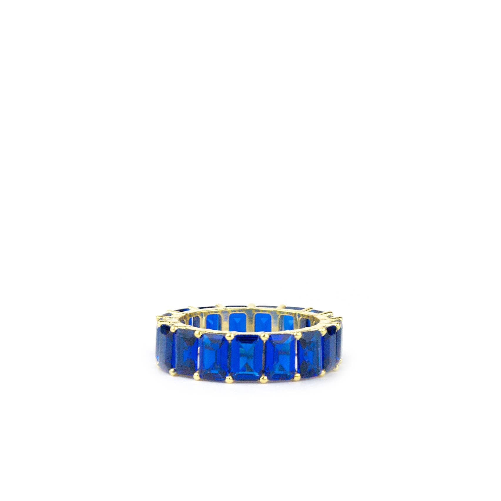 Introducing the Gold Plated Large Baguette Ring, a sophisticated piece highlighted by its stylish gold plating. This ring showcases a band of rectangular, faceted deep blue gemstones aligned side by side. The visible prongs enhance its intricate design, while the rich blue stones offer a stunning contrast to the gold band, creating an elegant and eye-catching appearance against a white background.