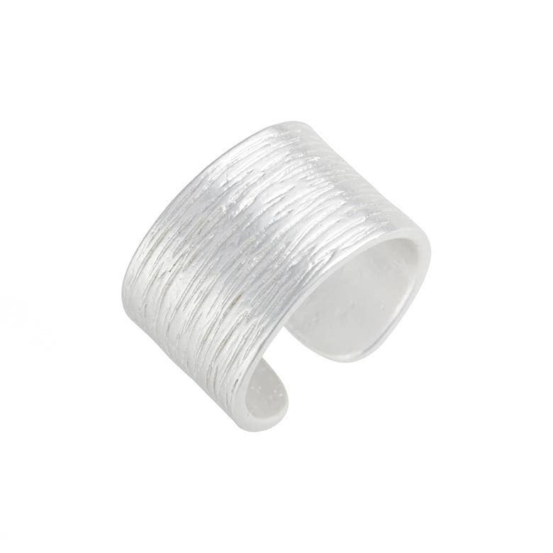 The Brushed Ring, renowned for its wide, silver-toned design and open-ended structure, is displayed against a plain white background. This minimalist piece showcases an elegantly curved form with a textured ridged surface and is accentuated by a contemporary 24 kt gold plating.