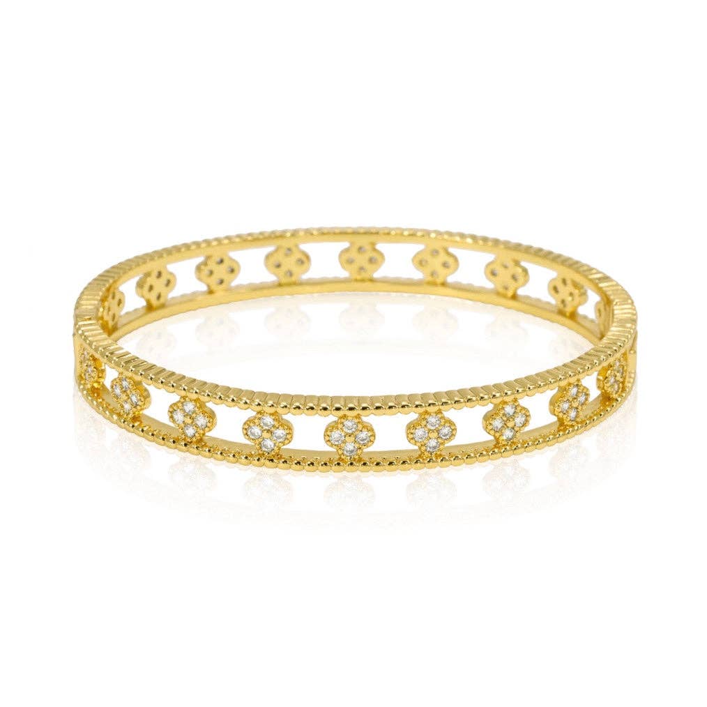The Gracie CZ Clover Bangle is a gold bracelet featuring a delicate openwork design with repeating floral motifs. This 18k gold-plated bangle is embellished with sparkling diamonds set within each flower, adding elegance. The polished surface shines brightly on a reflective white background.