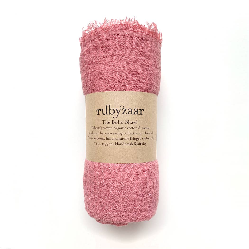 A hand-dyed pink shawl with fringe detailing is enveloped in a brown paper label that reads "rubyzaar." Referred to as "The Boho Scarf," this cotton and viscose accessory captures bohemian style, handcrafted in Thailand. It measures 72 by 39 inches and includes care instructions for hand washing and air drying.