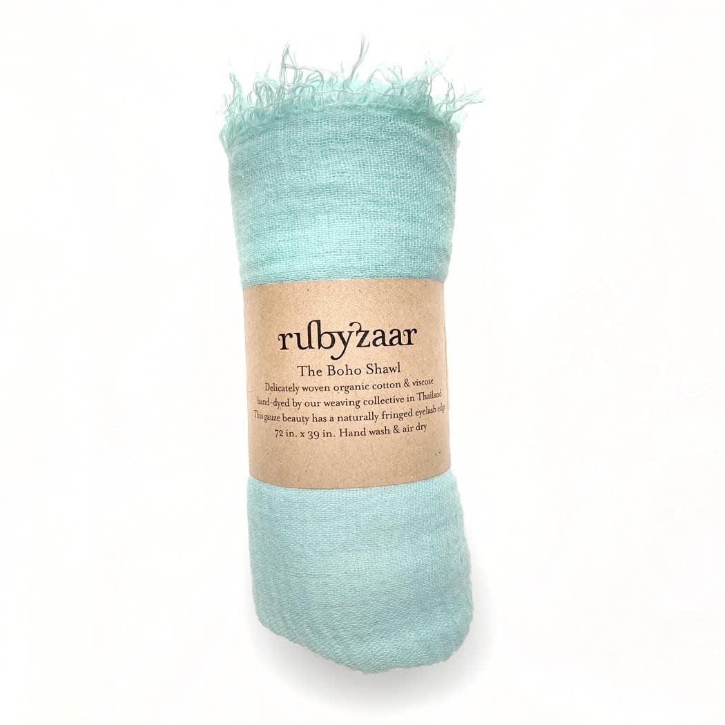 A rolled-up teal shawl with fringed edges is wrapped in a brown paper label reading "rubyzaar, Boho Scarf." Crafted from hand-dyed organic cotton and viscose, this bohemian style scarf measures 72 x 39 inches. It advises hand washing and air drying against the pristine white background.
