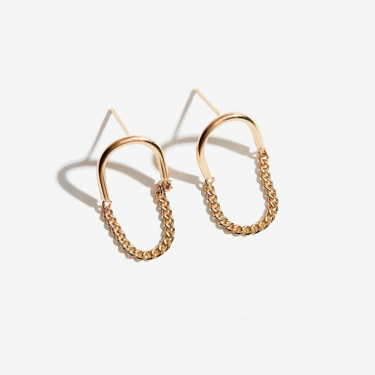 The Arc Chain Earrings showcase a stylish chain link design, featuring gold-filled hoops. The semi-circle structure highlights smooth, shiny metal on the upper half with an elegantly intertwined chain pattern beneath. Ideal for advocates of ethical fashion, these earrings are displayed against a light gray background, casting delicate shadows.