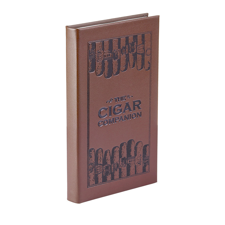 The image displays a brown bonded leather book titled "The Cigar Companion," ideal for cigar enthusiasts. It has embossed illustrations of handmade cigars on the front cover, arranged vertically around the title, which is presented in black uppercase letters. The spine of the book is also visible.