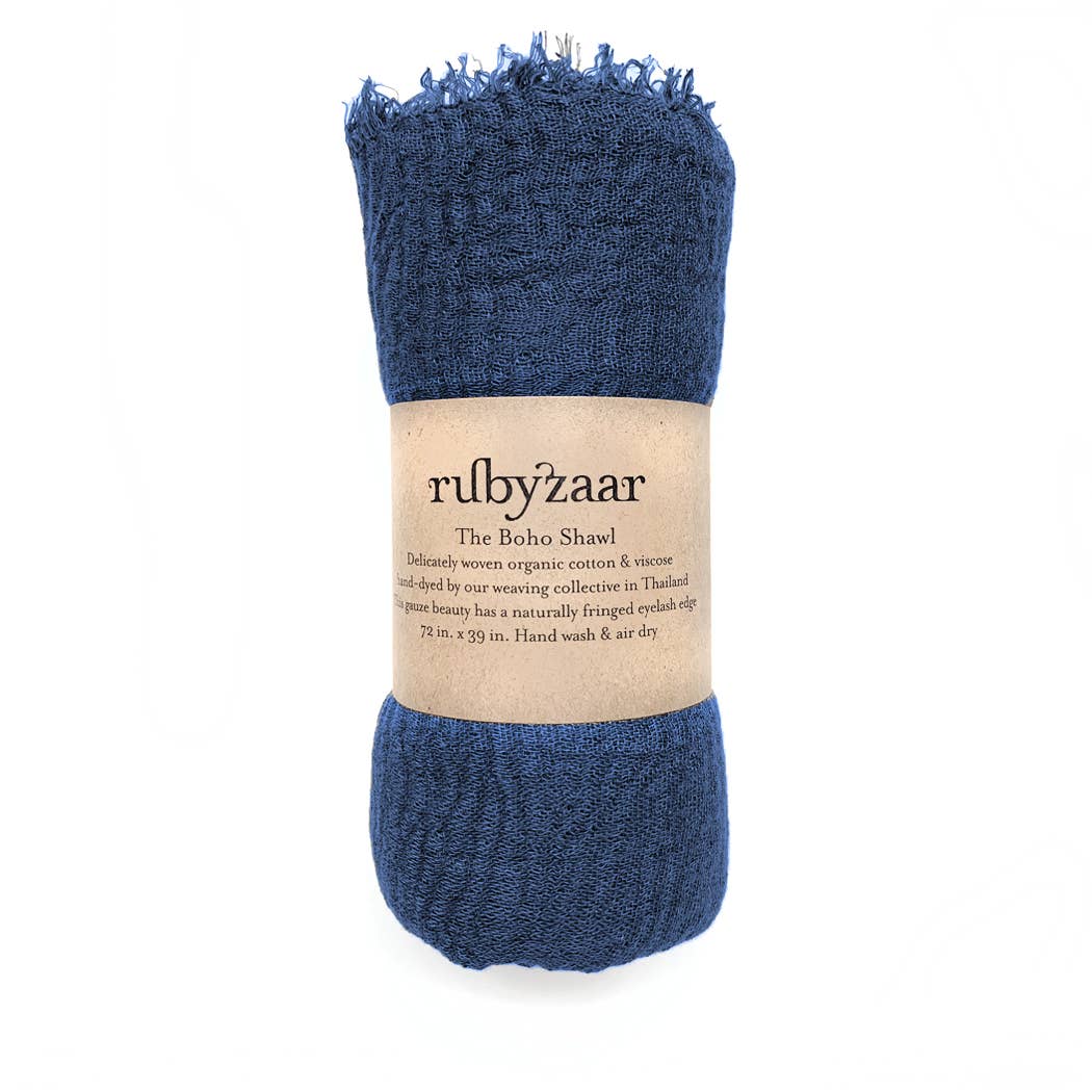 A blue woven scarf, embodying bohemian style, is rolled into a cylinder with a brown paper label that reads "rubyzaar Boho Scarf." Hand-dyed and crafted in Thailand from cotton and viscose, it measures 78 inches by 29 inches. Care instructions suggest hand washing and air drying.