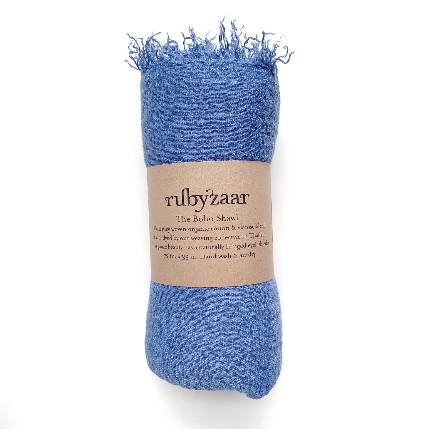 A rolled-up blue Boho Scarf with frayed edges is wrapped in a brown paper label. The label reads: "rubyzaar - Bohemian Style Scarf - Delicately woven organic cotton & viscose blend, hand dyed by our weaving collective in Thailand. This azure beauty has a naturally fringed eyelash edge. 72 in. x 29 in. Hand wash & air dry.