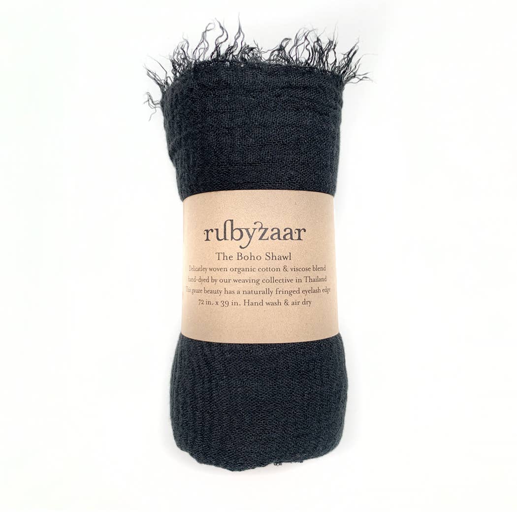 A rolled-up, dark-colored Boho Scarf with a fringed edge is encircled by a brown paper band labeled "rubyzaar: The Boho Shawl." This item is described as handmade from organic cotton and viscose, hand-dyed in Thailand. With dimensions of 72x39 inches, it’s recommended to hand wash and air dry.