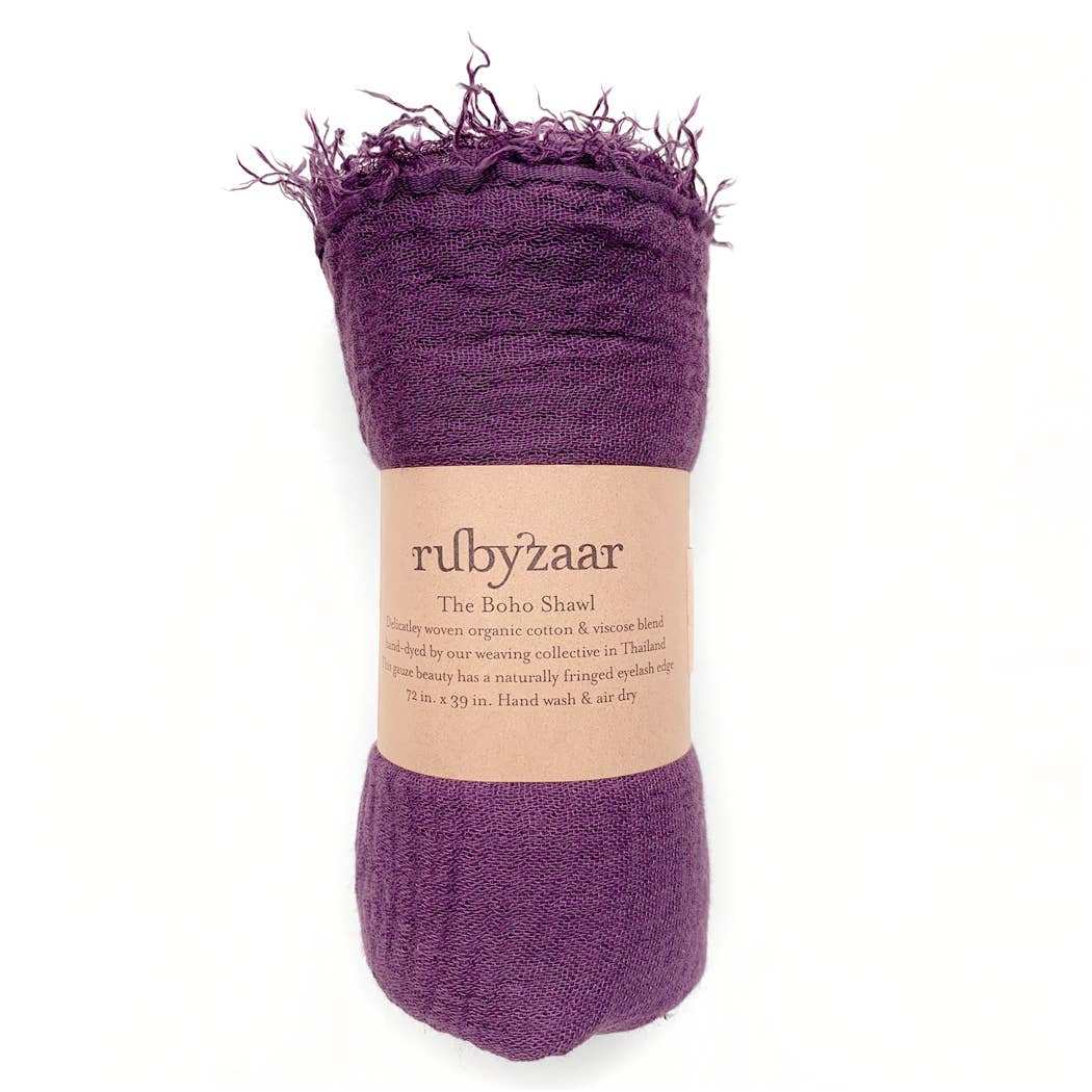 A rich purple bohemian-style scarf with a fringed edge is rolled up and wrapped in a brown paper label. The label reads, "rubyzaar The Boho Scarf," emphasizing its hand-woven blend of organic cotton and viscose, made in Thailand. It measures 72 x 39 inches and comes with instructions for hand washing and air drying.