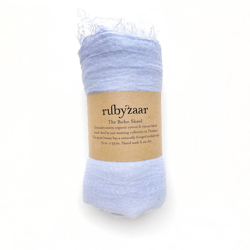 A light blue, bohemian style scarf is rolled up with a brown paper label wrapped around it. The label reads "rubyzaar" and "Boho Scarf," highlighting that it's handmade in Thailand from cotton and viscose. This hand-dyed piece measures 72 inches by 39 inches, emphasizing its fair-dry qualities.