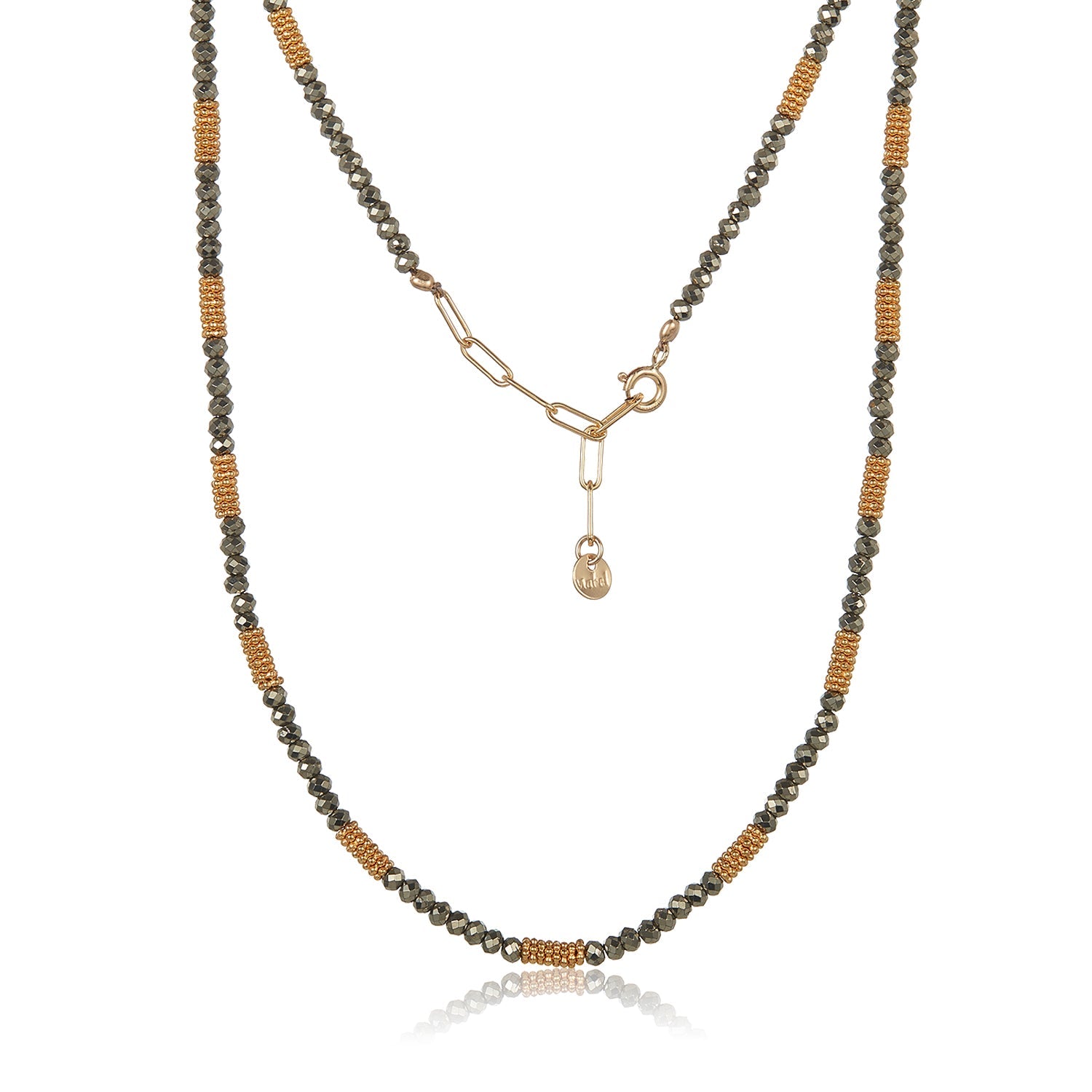 The Pyrite Choker is a stunning beaded necklace that showcases alternating sections of small, metallic grey pyrites and clusters of gold-colored beads elegantly strung on a silk cord. It includes a gold chain extension with an adjustable clasp and is adorned with a small, oval tag. The choker is beautifully displayed on a white background.