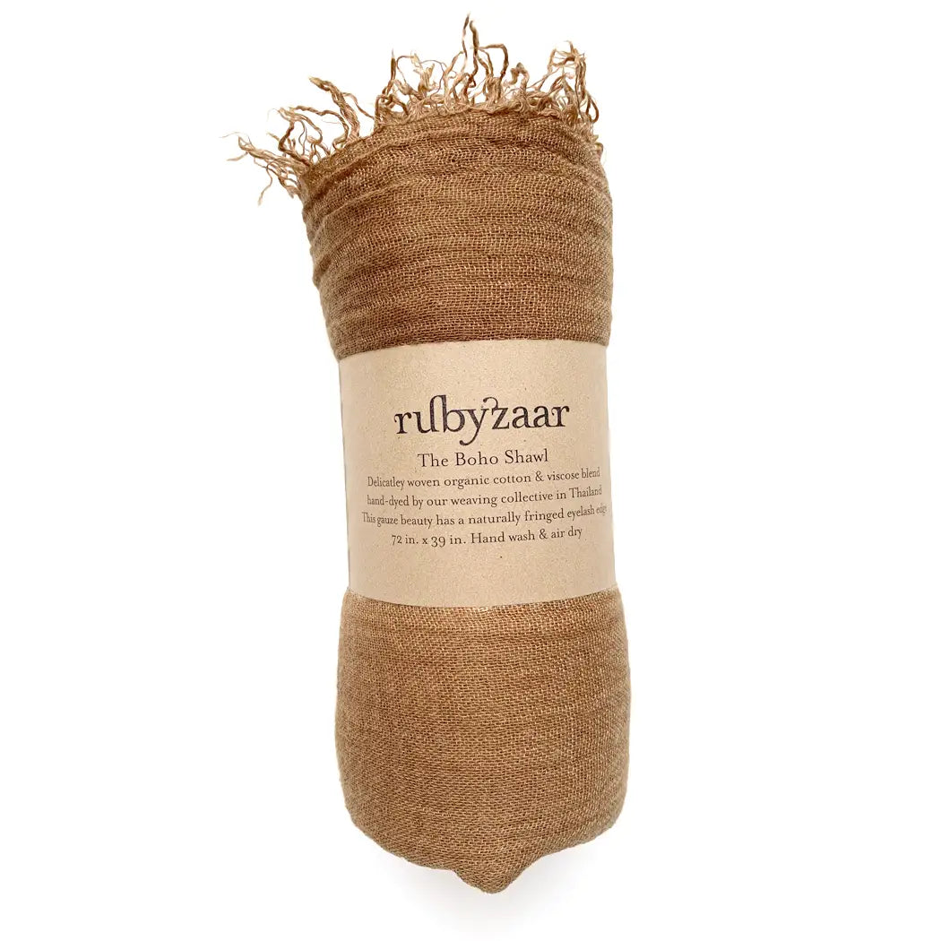 A rolled-up brown shawl with fringed ends, wrapped in a label reading "rubyzaar, Boho Scarf." This bohemian style scarf is crafted from a luxurious blend of cotton and viscose, hand-dyed and handwoven in Thailand. It measures 28 inches by 79 inches and comes with instructions recommending hand washing and air drying.